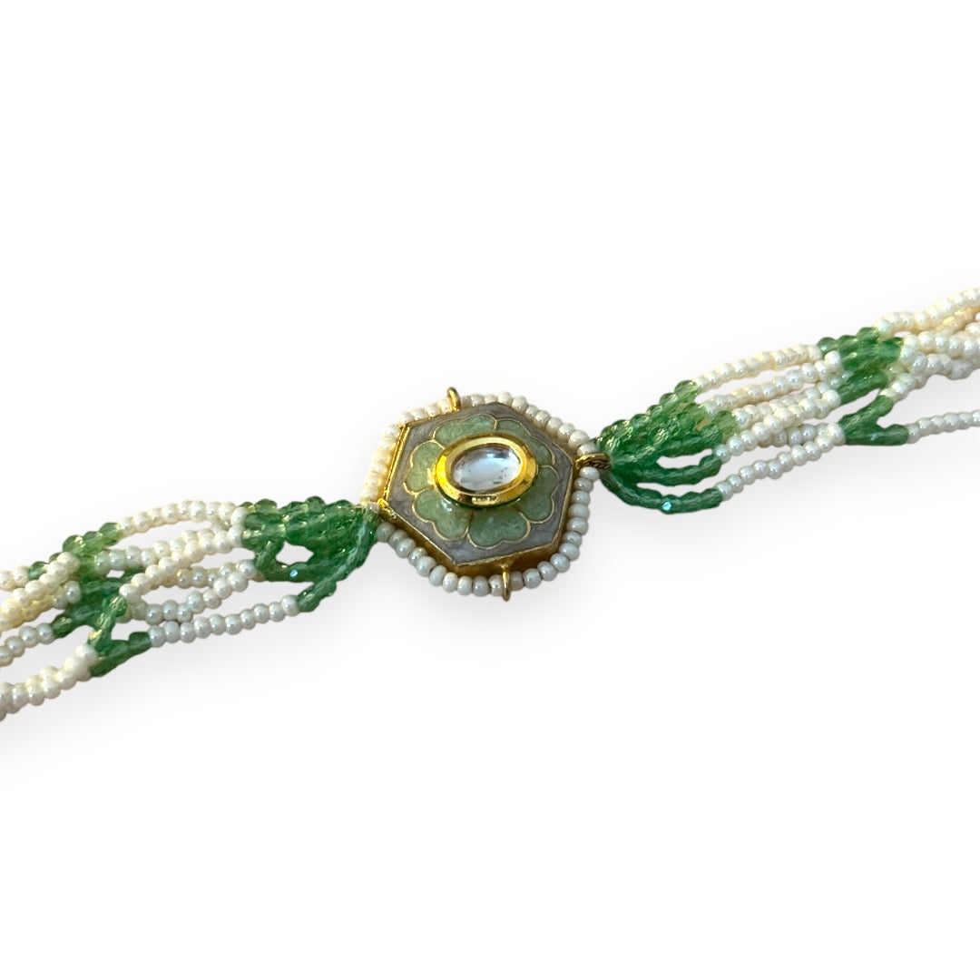 The Marguerite Bracelet features a bold hexagonal shape, surrounded by delicate Kundan stones and lustrous pearls. Elegant green enamel hand-painted to perfection brings a striking contrast to the bracelet, while green and white chains on either side create a harmonious balance of color and texture.