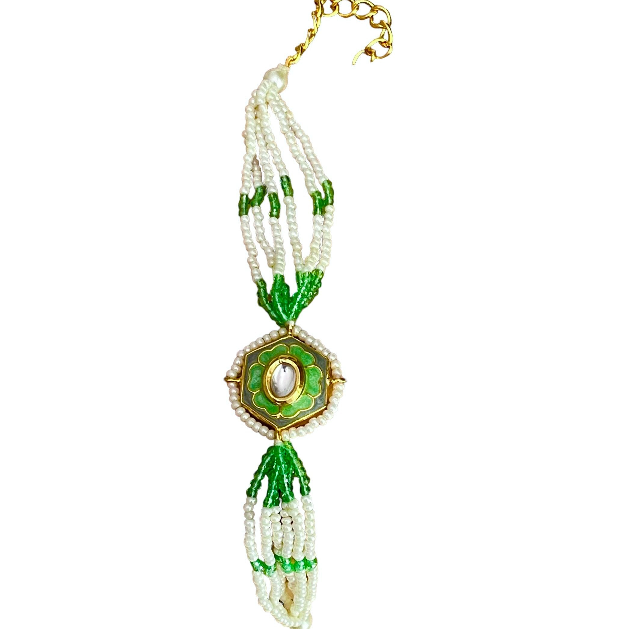 The Marguerite Bracelet features a bold hexagonal shape, surrounded by delicate Kundan stones and lustrous pearls. Elegant green enamel hand-painted to perfection brings a striking contrast to the bracelet, while green and white chains on either side create a harmonious balance of color and texture.