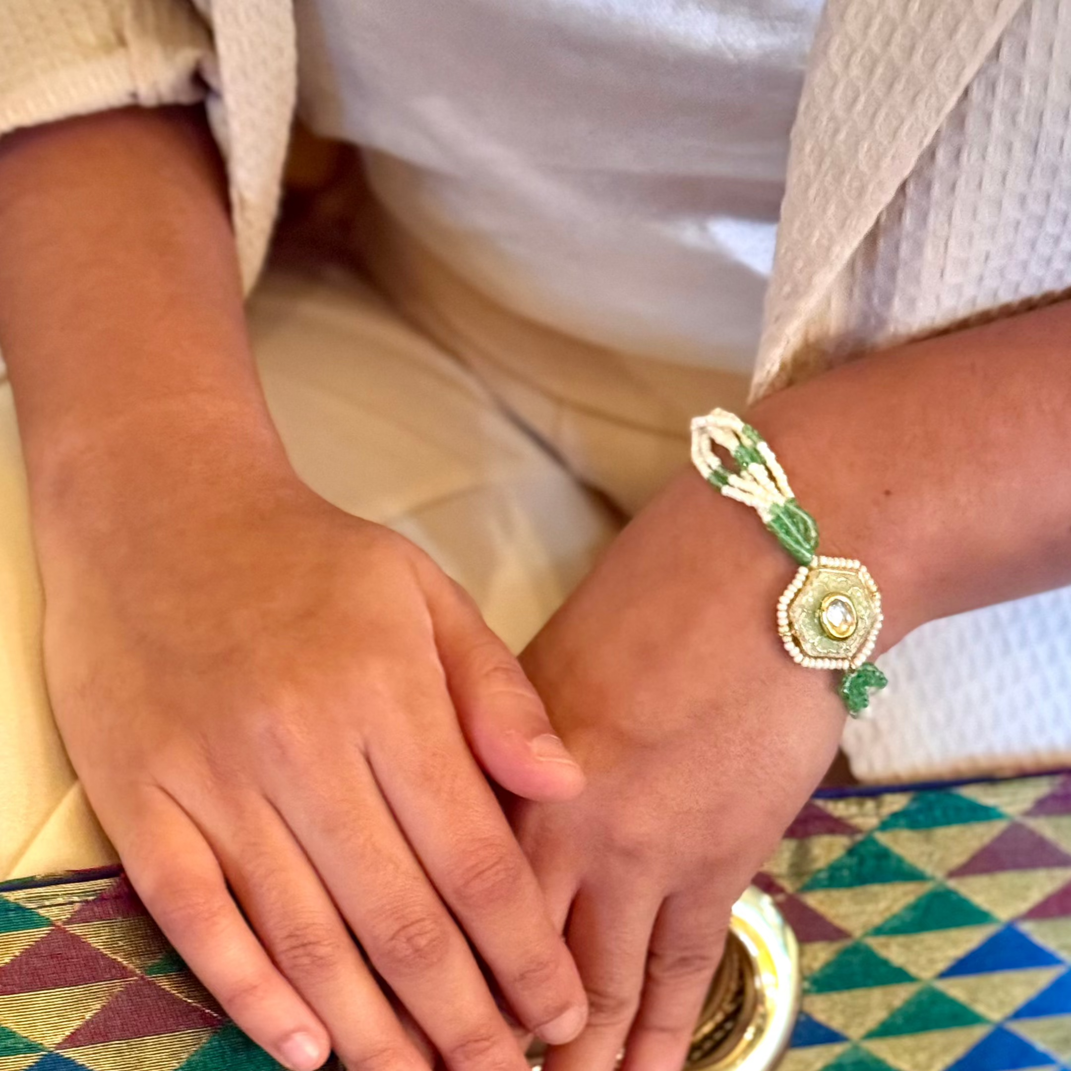 The Marguerite Bracelet features a bold hexagonal shape, surrounded by delicate Kundan stones and lustrous pearls. Elegant green enamel hand-painted to perfection brings a striking contrast to the bracelet, while green and white chains on either side create a harmonious balance of color and texture.