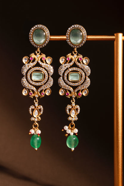 Ornate earrings with green gemstones and gold accents on a dark background