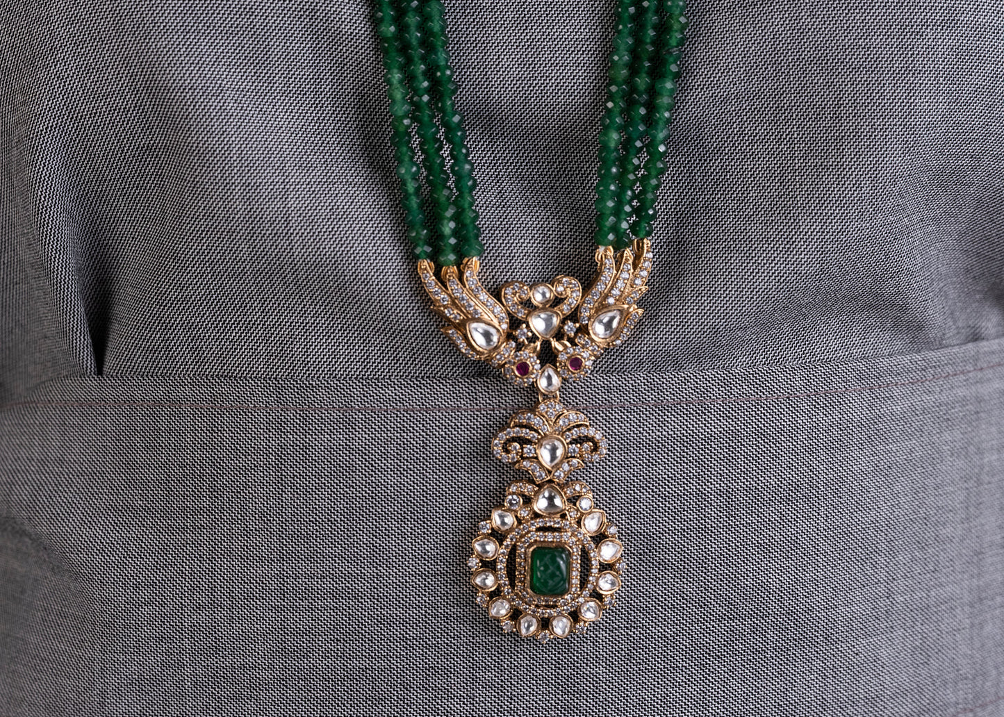 Decorative necklace with green beads and a pendant on a gray fabric background
