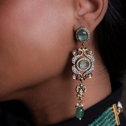 Close-up of an ornate earring with gemstones on a person wearing a black outfit with green jewelry.