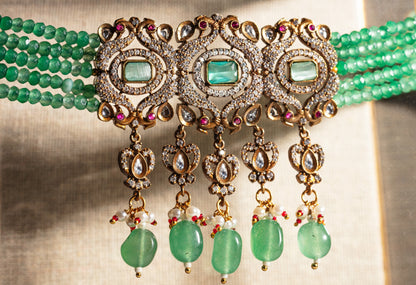 Ornate necklace with green beads and gold accents on a textured background
