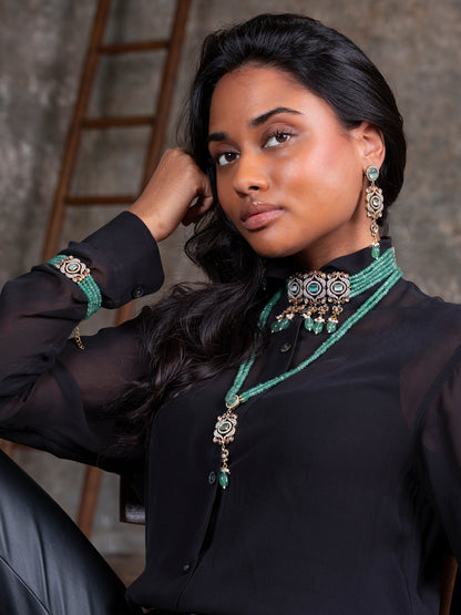 Woman wearing black attire with green jewelry against a textured wall.
