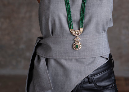 Person wearing a gray outfit with a green beaded necklace and black pants.