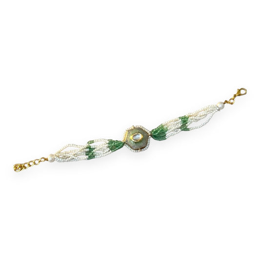 The Marguerite Bracelet features a bold hexagonal shape, surrounded by delicate Kundan stones and lustrous pearls. Elegant green enamel hand-painted to perfection brings a striking contrast to the bracelet, while green and white chains on either side create a harmonious balance of color and texture.