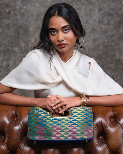 Woman holding a patterned handbag on a brown leather couch with a gray background