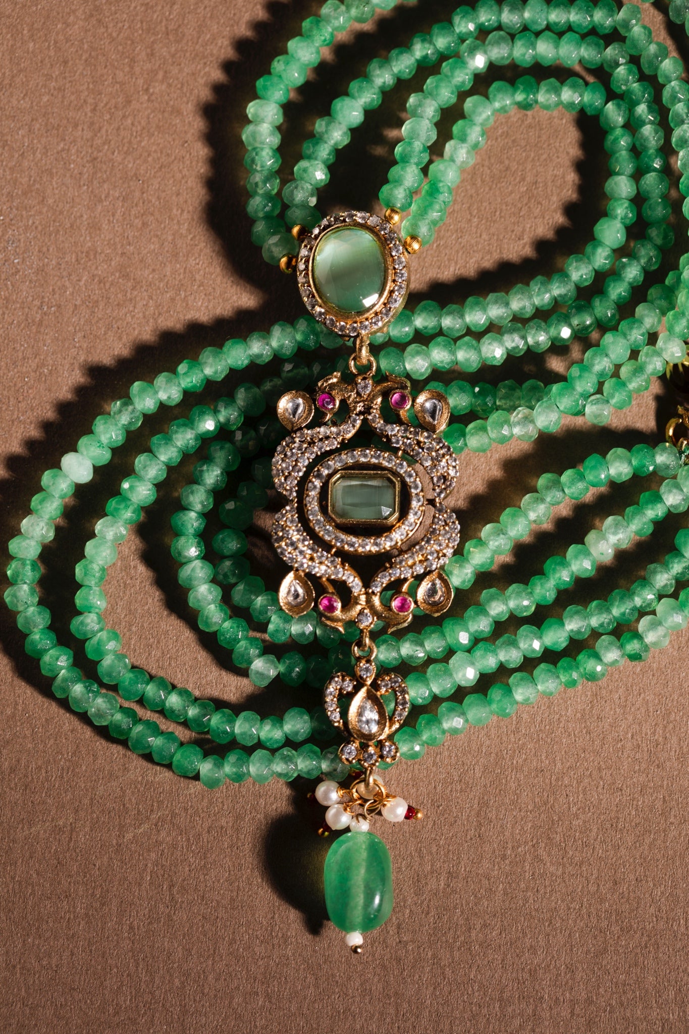 Green beaded necklace with decorative pendant on a brown background